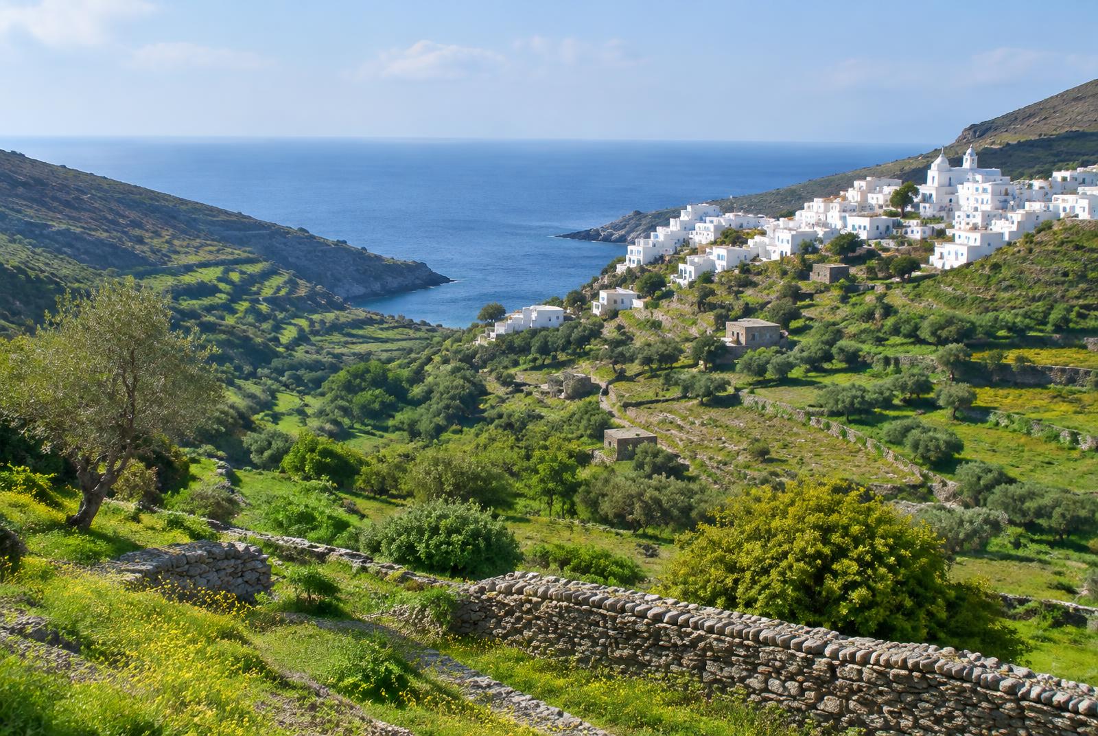 Grünes Tal mit Steinmauern und einem weißen Dorf, im Hintergrund das Meer