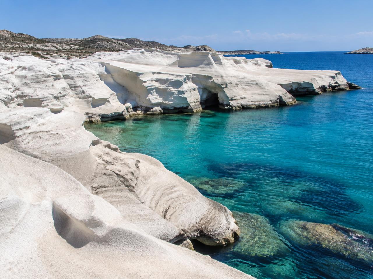 Weiße, vom Wind geformte Vulkanfelsen an einer türkisen Bucht auf Milos